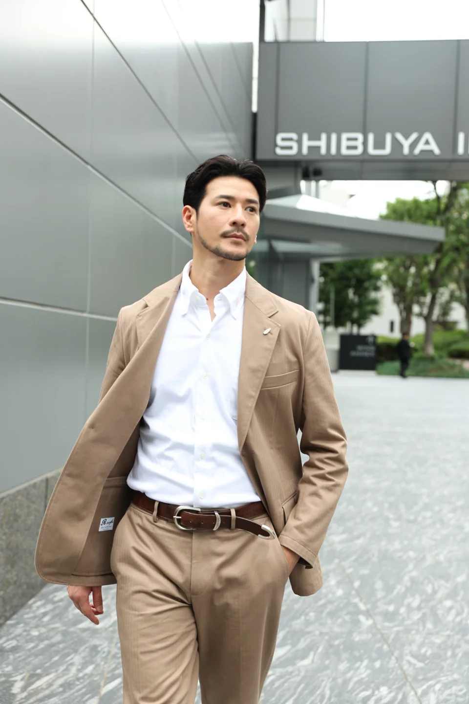 ブラウンのジャケットとパンツを街中で着用したスタイル